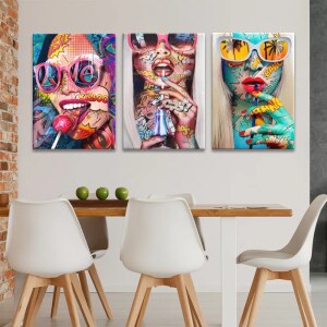 Tableau visage pop art femmes à lunettes affiché sur le mur blanc d'une cuisine avec mur en pierre et table en bois assortie de chaises blanches modernes